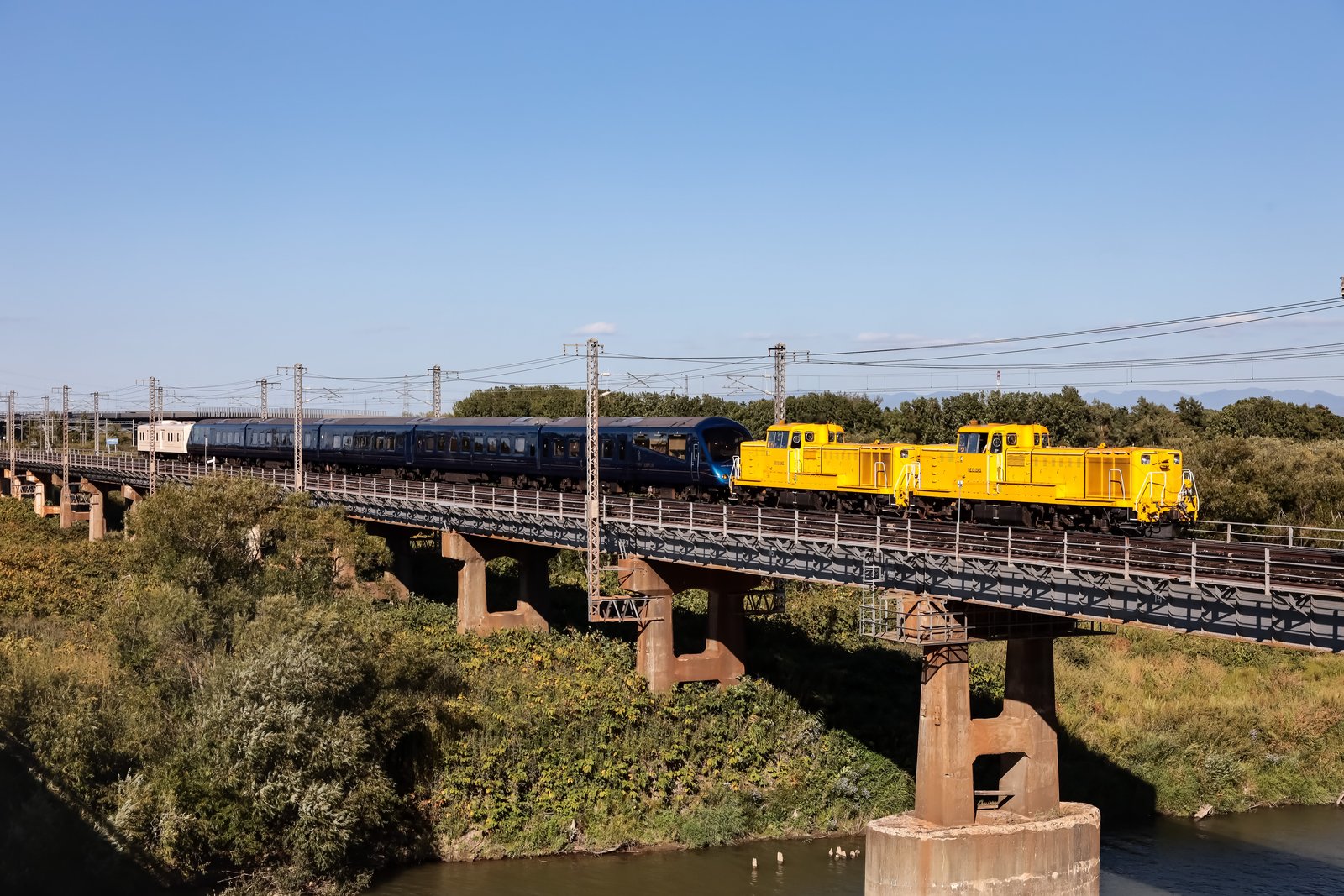 鉄橋の上を、黄色いディーゼル機関車2両に引かれて走る青いTHE ROYAL EXPRESS。青空の下、川と草地の上を渡る