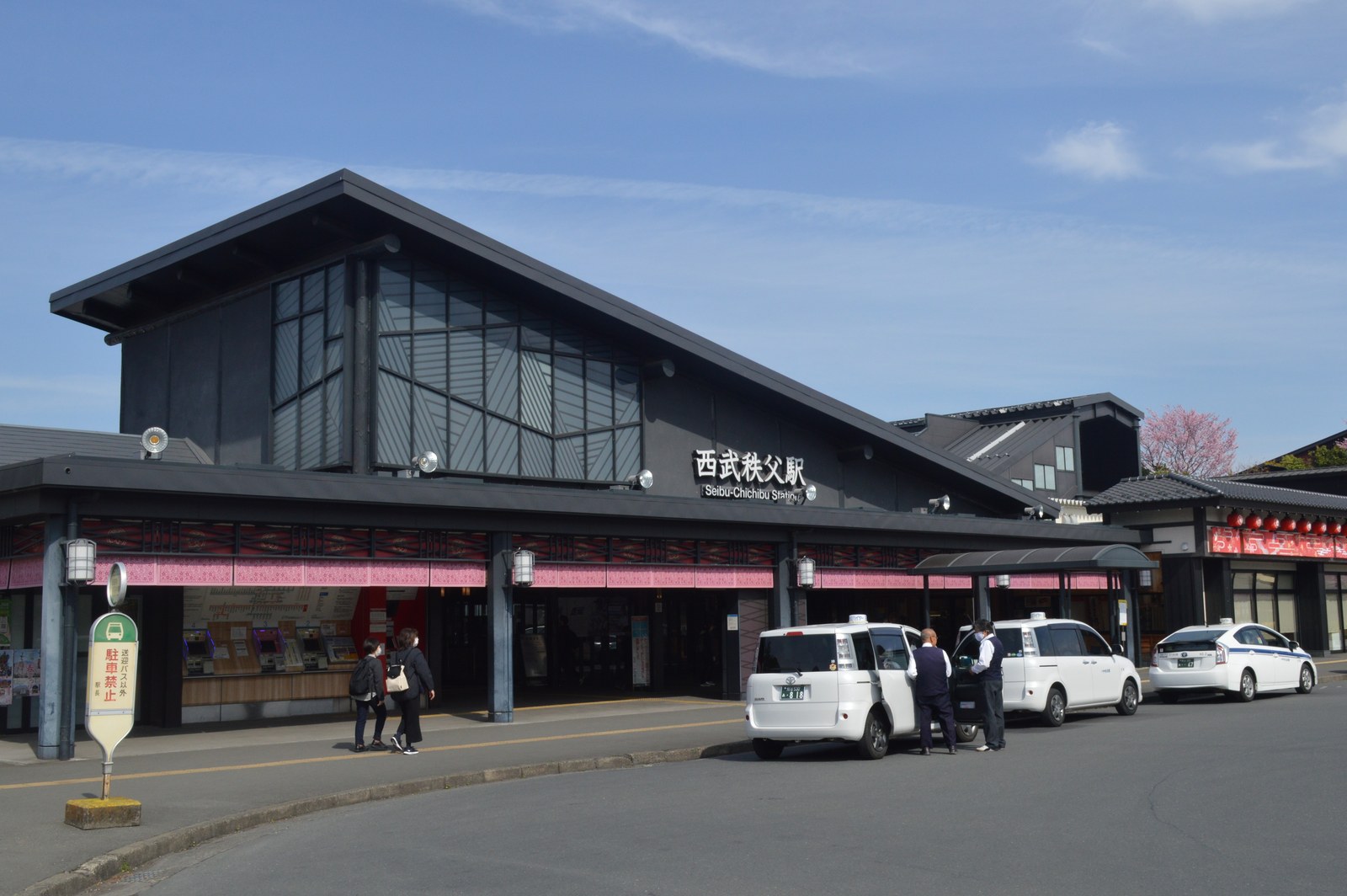 西武秩父駅の駅舎。黒い大きな片流れの屋根の下に駅名の文字があり、駅前にタクシーが並んでいる