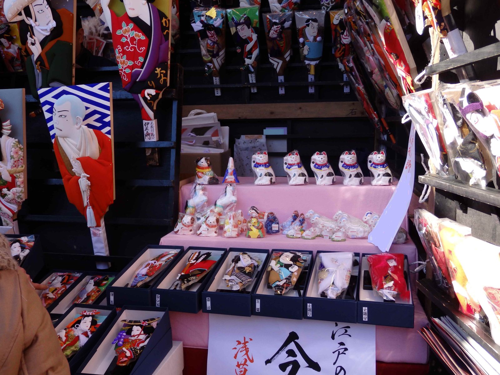 羽子板市の露店。歌舞伎の役者の姿を布で立体に仕立てた押絵羽子板が壁に並び、台の上に招き猫の人形が置かれている