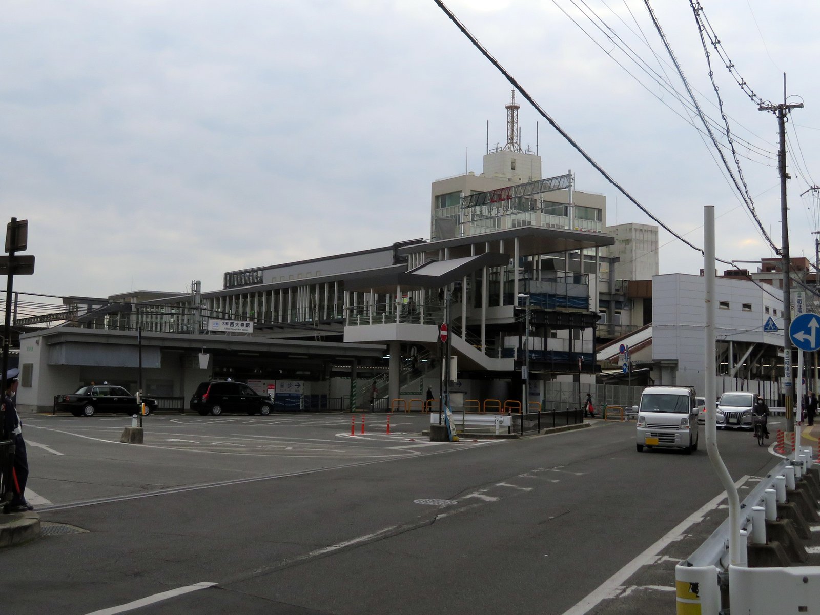 近鉄大和西大寺駅の駅前。高架の通路と階段が駅舎から延び、手前にロータリーとタクシー、「大和西大寺駅」の看板