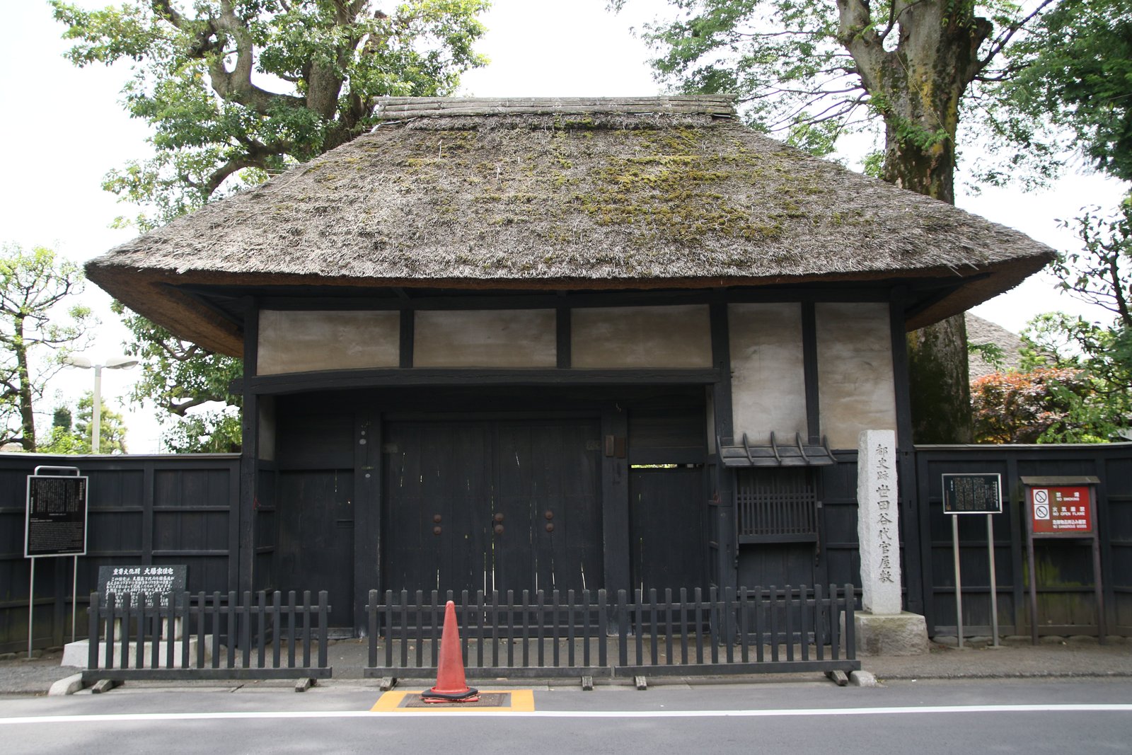 世田谷代官屋敷の表門。茅葺きの屋根に黒い板壁の門で、右手に名を刻んだ石柱が立つ