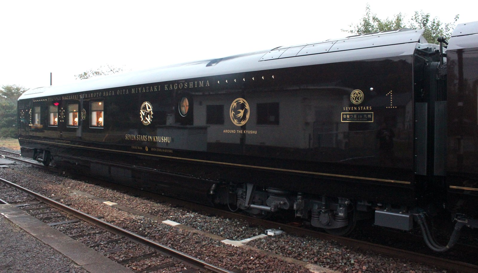 阿蘇駅に停まるななつ星in九州の1号車。濃いワインレッドの車体に金色の「SEVEN STARS IN KYUSHU」の文字と星の紋章、車端に大きな「1」の数字が入る