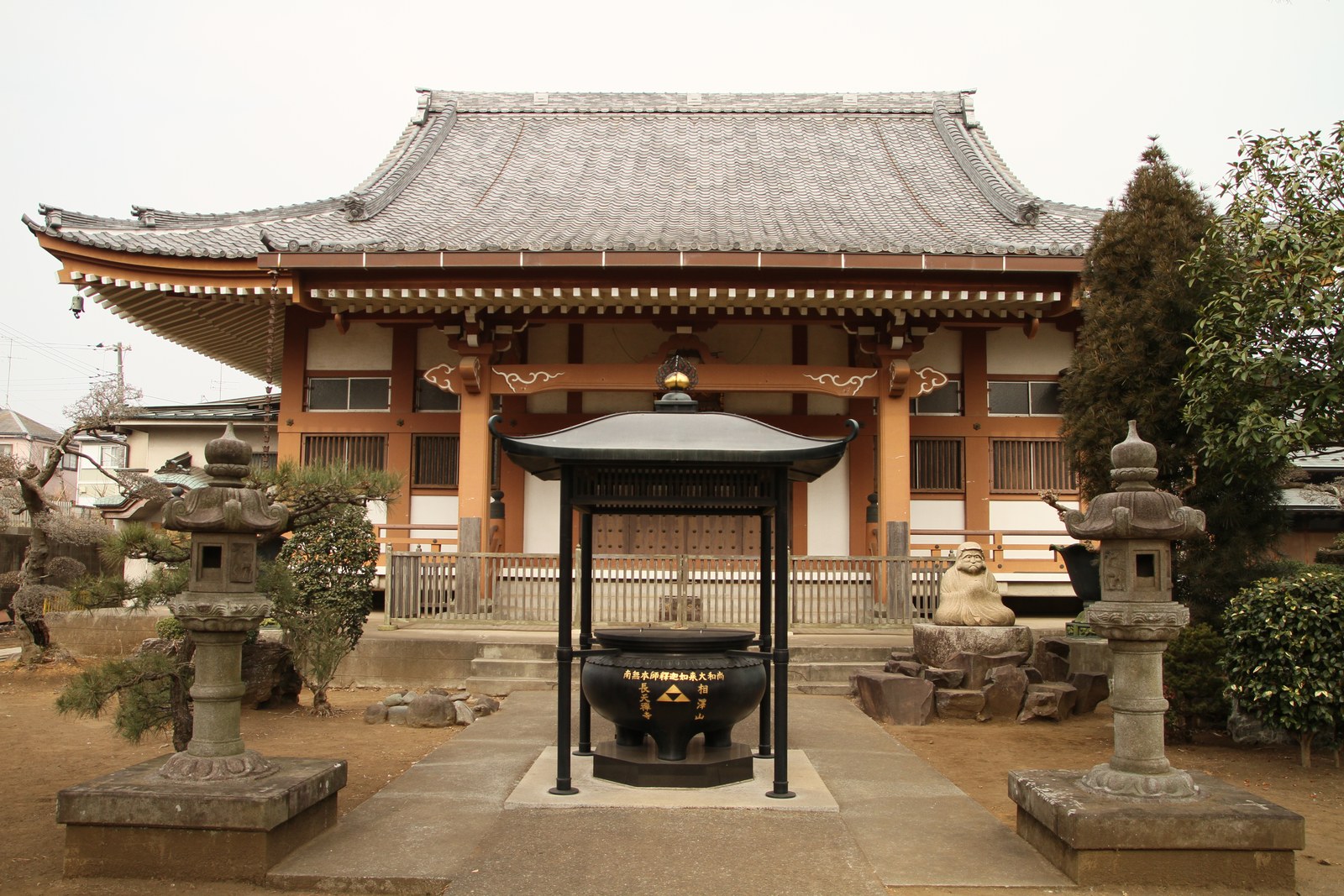 長天寺の本堂。瓦屋根の木造の本堂の前に、屋根の付いた香炉と石灯籠が 2 基ある