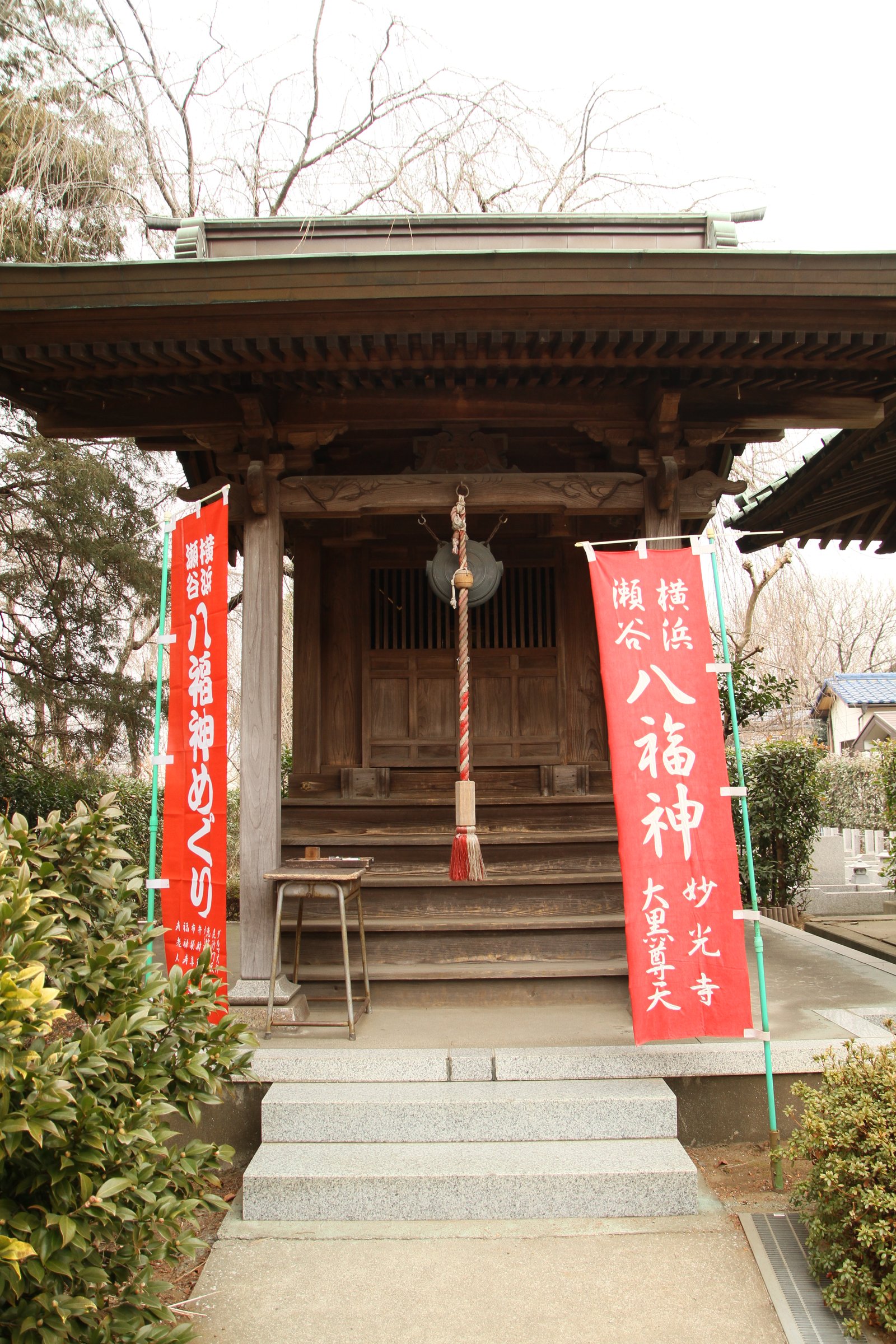 妙光寺の大黒天堂。木造の堂の前に「横浜瀬谷八福神めぐり」「妙光寺 大黒尊天」と書いた赤いのぼりが 2 本立ち、軒下に鰐口と鈴の緒が下がる