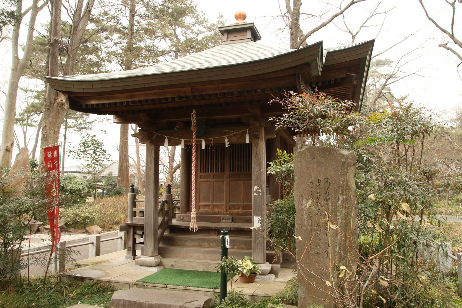 徳善寺の毘沙門堂。木立の中に建つ銅板葺きの屋根の小さな堂で、正面の柱に注連縄と鈴の緒が掛かり、右手前に石碑が立つ