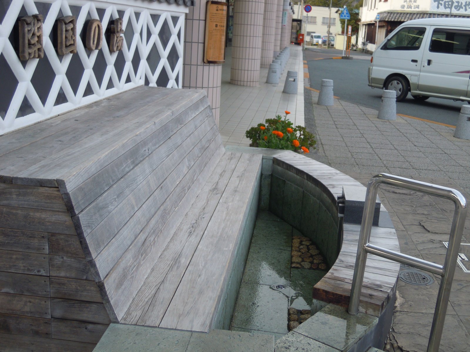 伊豆急下田駅前の足湯。「開国の湯」の文字が掲げられた壁の前に木のベンチが据えられ、足を入れる浅い湯の溝が弧を描いて続いている