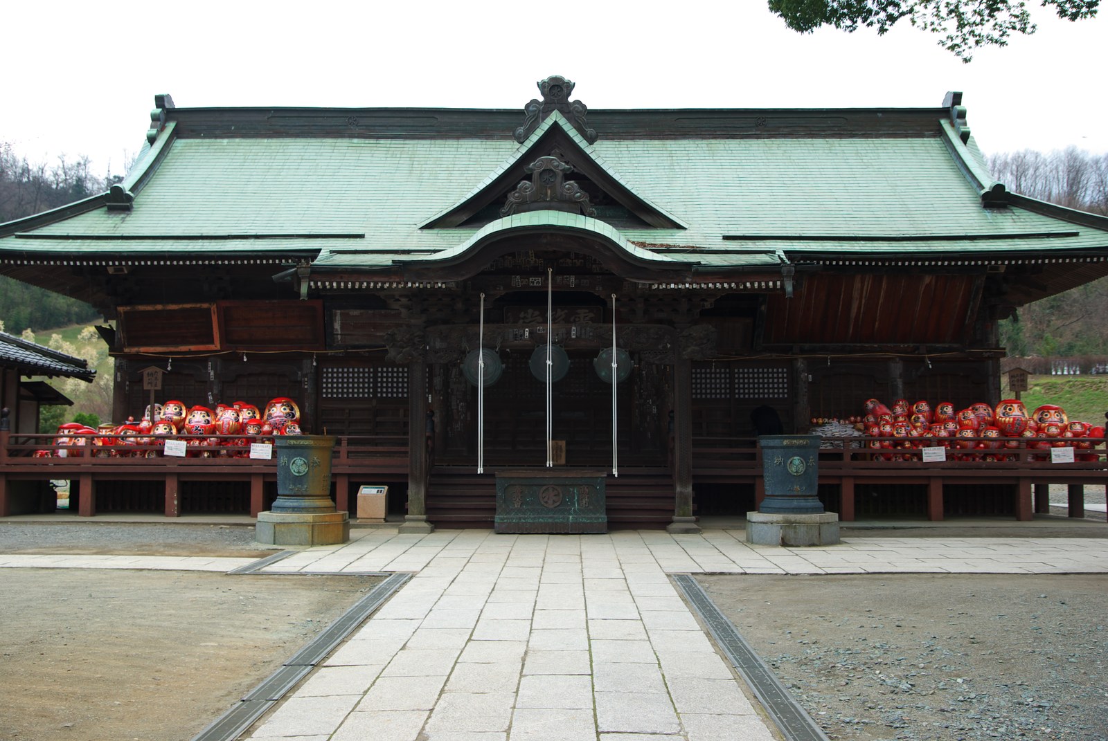 少林山達磨寺の本堂。緑の屋根の堂の縁に、納められた赤いだるまが山のように積まれている