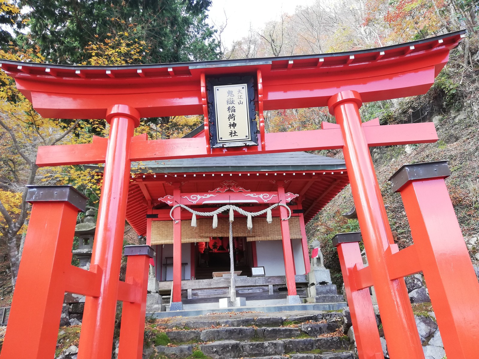 大江山の鬼嶽稲荷神社。赤い鳥居の奥に朱塗りの社殿があり、鳥居の扁額に「鬼嶽稲荷神社」と書かれている