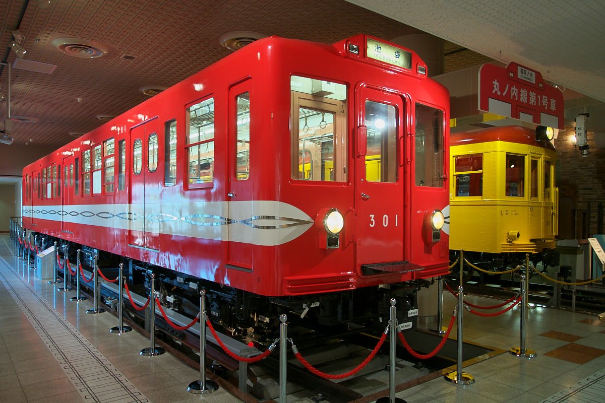 赤い車体の丸ノ内線301号車の正面、奥に1001号車、「丸ノ内線第1号車」の案内板