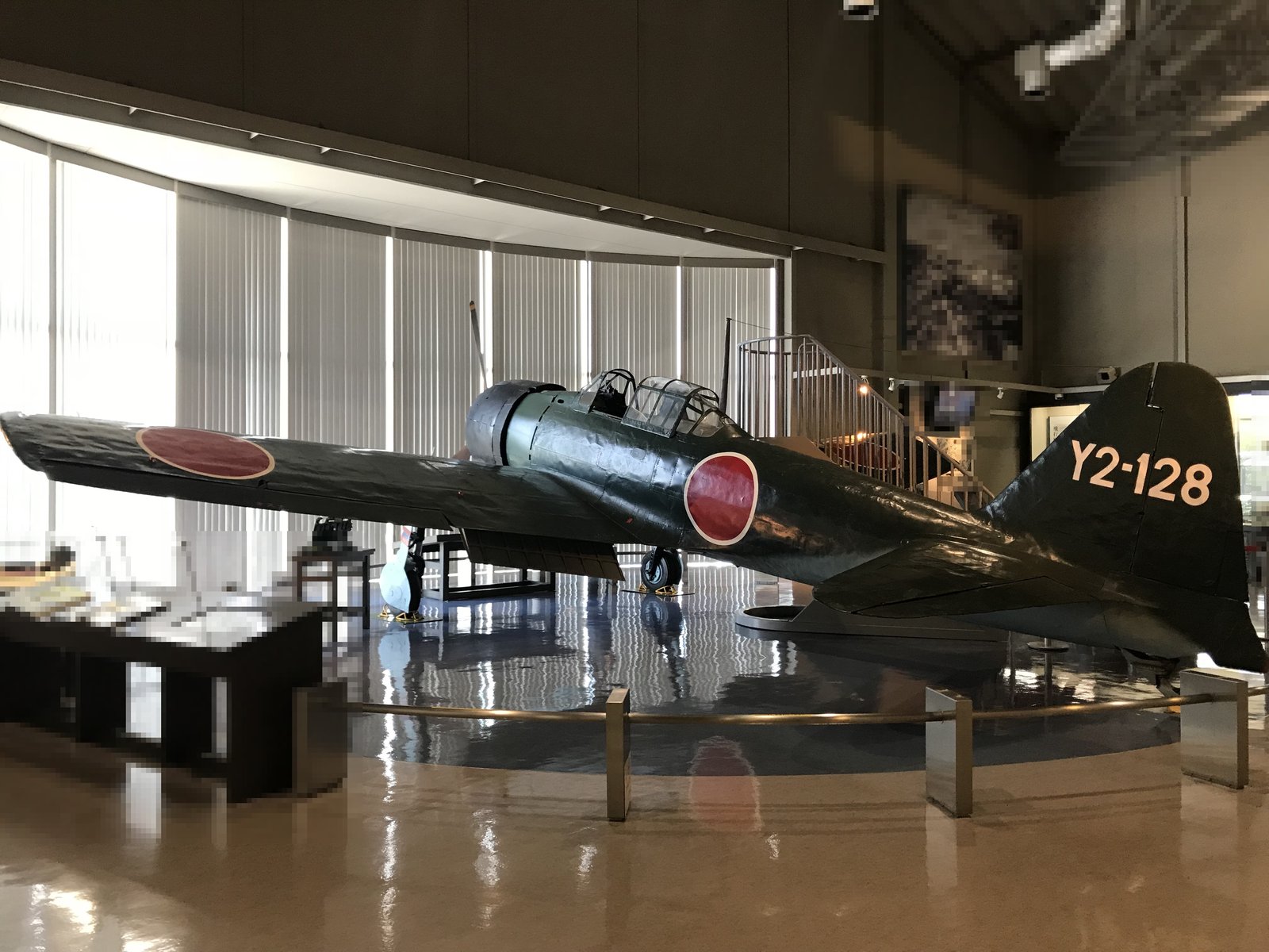 展示室の床に置かれた濃い緑色の零戦。主翼と胴体に赤い日の丸があり、尾翼に白い文字で「Y2-128」と書かれている