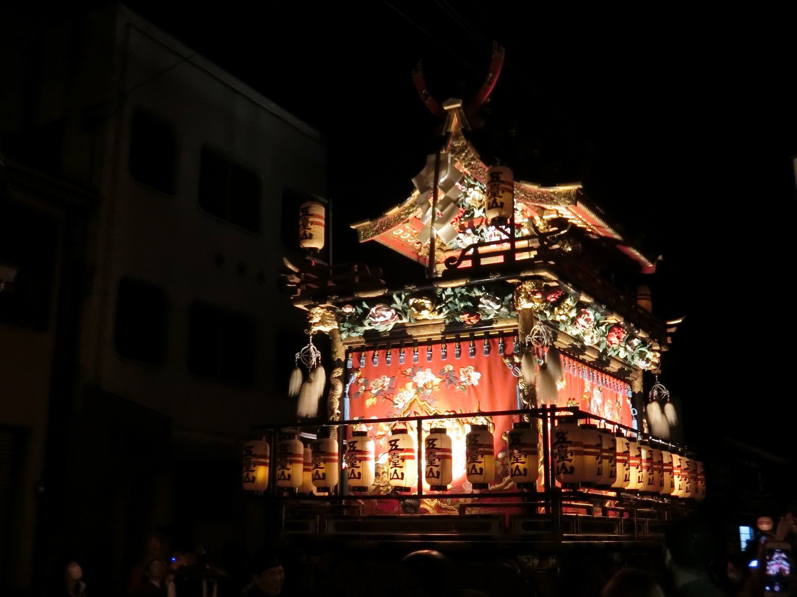 夜の高山祭で提灯を灯した屋台。「五臺山」と書いた提灯が下段に並び、赤い幕と金色の屋根飾りが暗い町並みの中に浮かんでいる