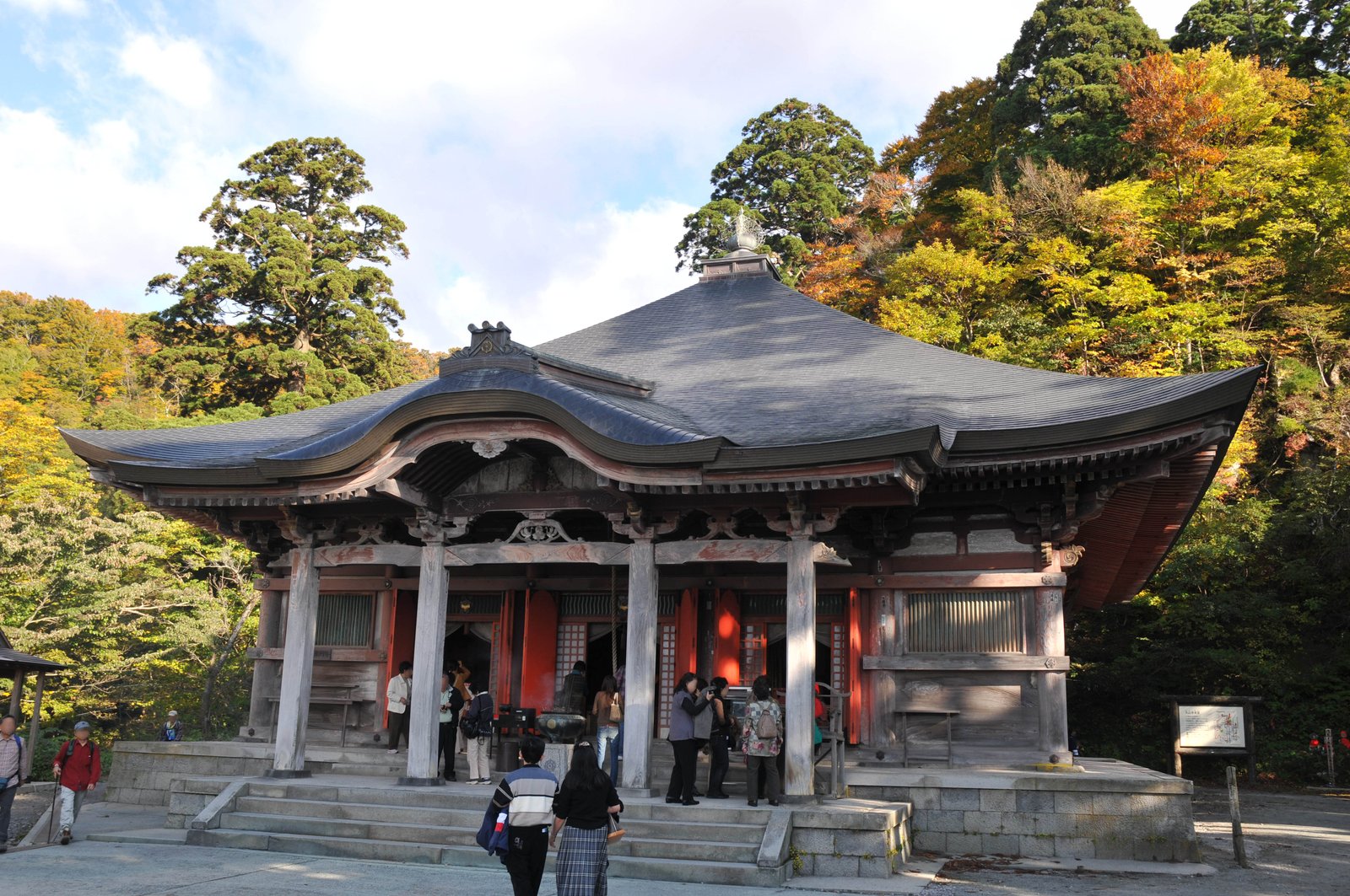 大山寺の本堂。反りのある大きな瓦屋根と白木の柱、朱塗りの扉が並び、背後に色づき始めた山の木々が見える