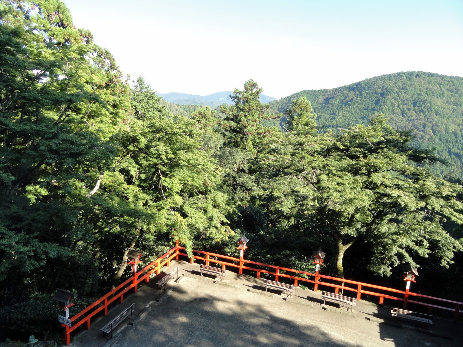 鞍馬寺境内の朱塗り高欄付き展望テラス。手前に朱色の玉垣と灯籠、ベンチが並び、奥に鞍馬山系の山並みが広がる