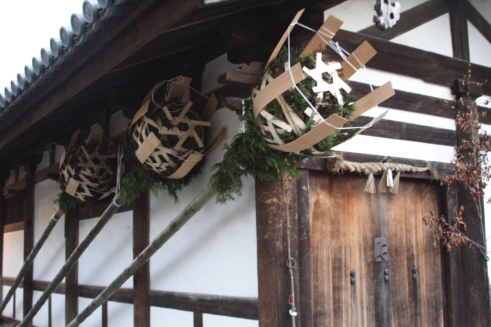 白壁の建物の軒に掛けられた3本の松明。長い竹の先に杉の葉と薄い木の板を籠のように組んだ玉が付き、扉の上に注連縄が張られている