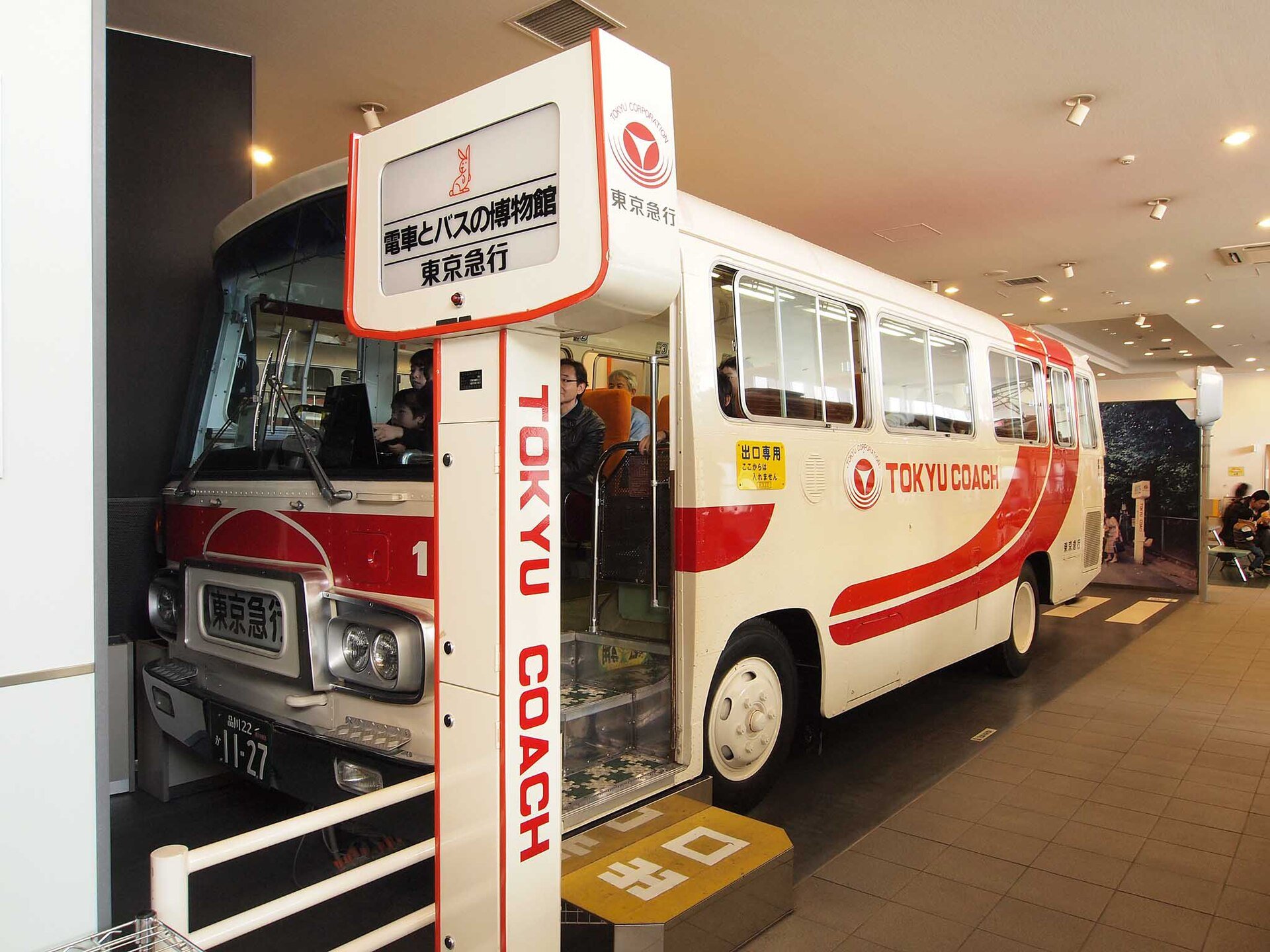 「電車とバスの博物館」の案内板と、赤と白の東急コーチのバス