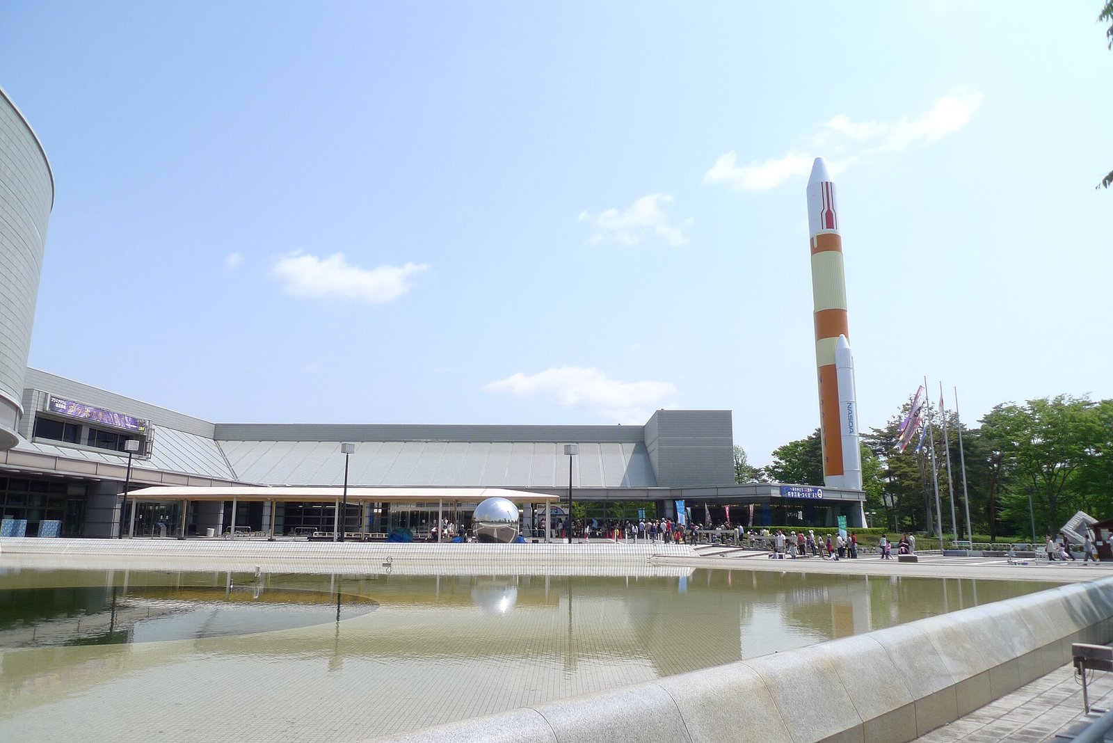 つくばエキスポセンターの屋外展示場に立つH-IIロケットの実物大模型。オレンジと白に塗られた塔がエントランス脇にそびえる