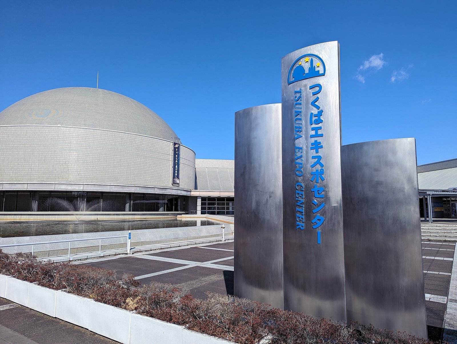 「つくばエキスポセンター TSUKUBA EXPO CENTER」の銘板と、その奥に立つ銀色のドーム型プラネタリウム棟