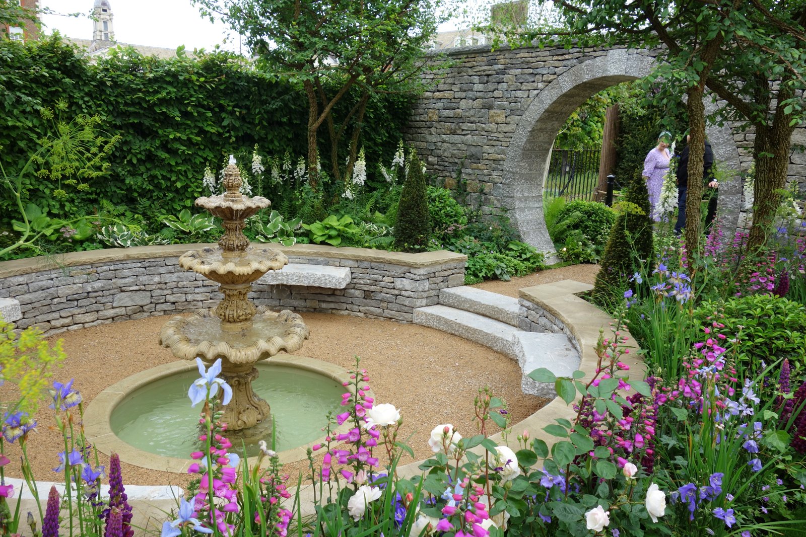 チェルシーフラワーショーの展示庭園。噴水を囲む花壇と石のアーチ