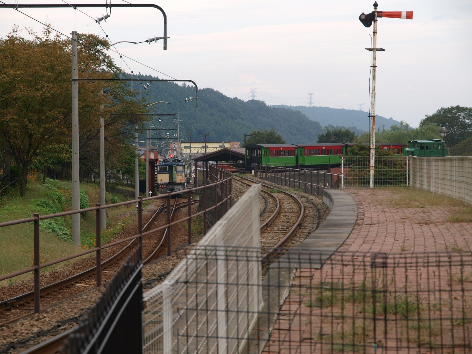 碓氷峠鉄道文化むら園内の線路を進む緑色の車両と、脇に立つ赤白の腕木式信号機、奥に山並み