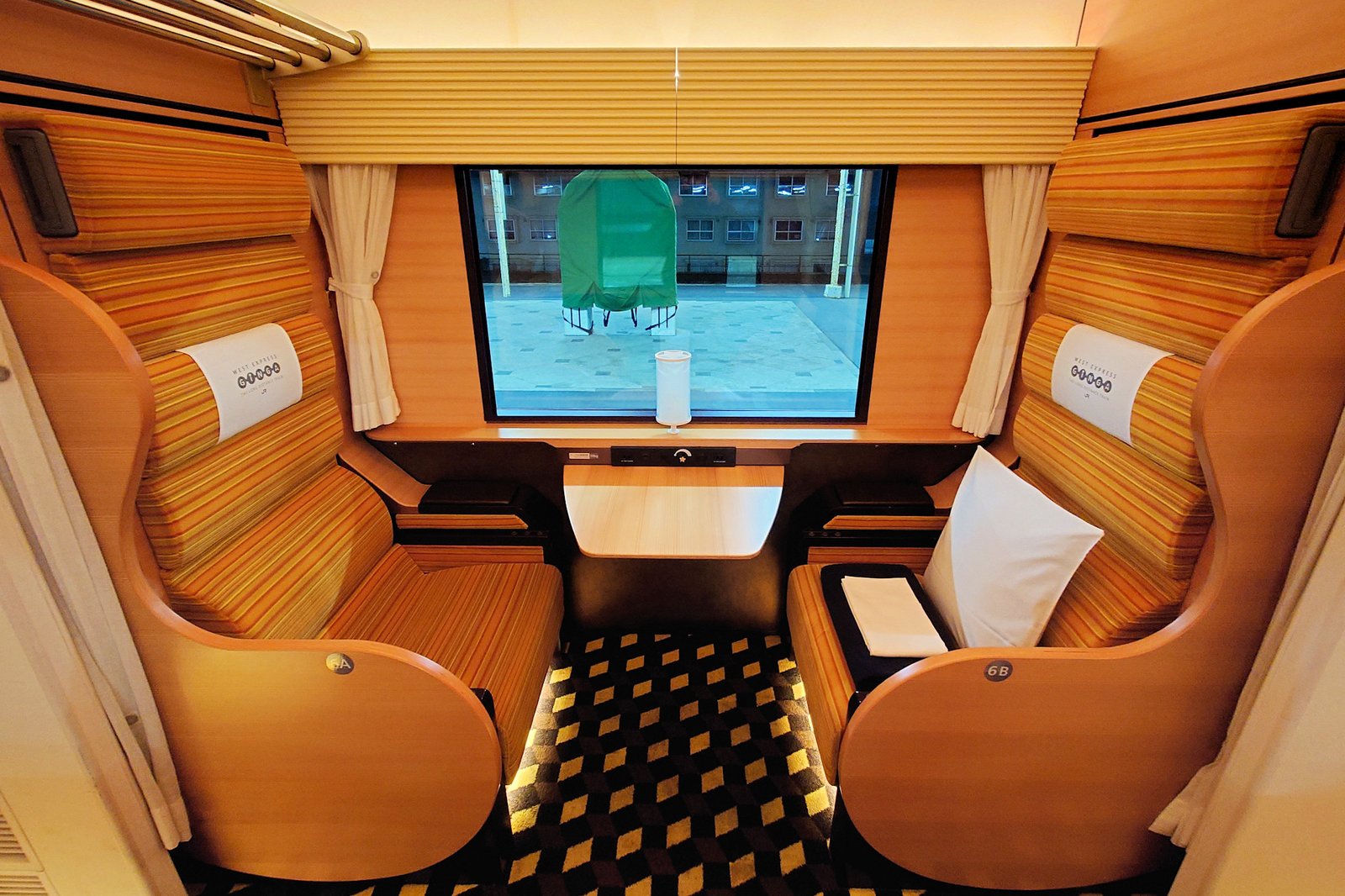 WEST EXPRESS 銀河の1号車ファーストシート。木目の背もたれの高い座席が窓をはさんで向かい合い、間に小さな机がある