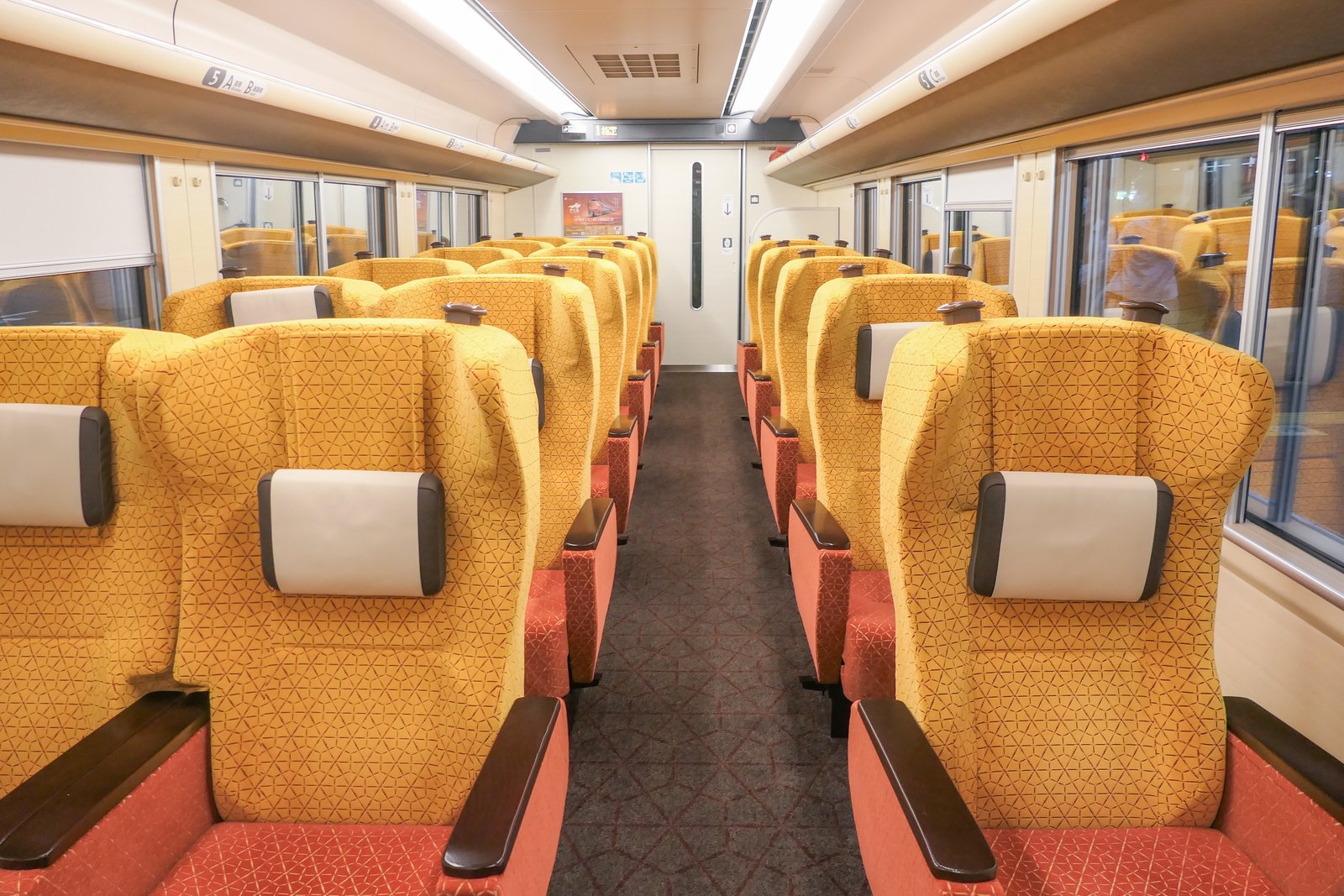 273系のグリーン車の車内。黄色い布地に赤い座面の座席が通路をはさんで2列ずつ並び、各席に白い枕が付く