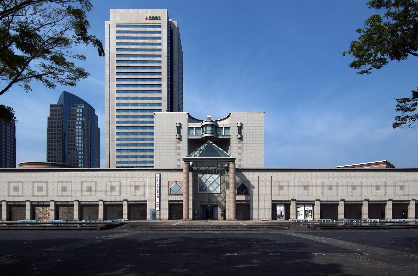 横浜美術館の正面。左右に長く伸びる石張りの建物の中央に塔があり、後ろに横浜ランドマークタワーが立つ