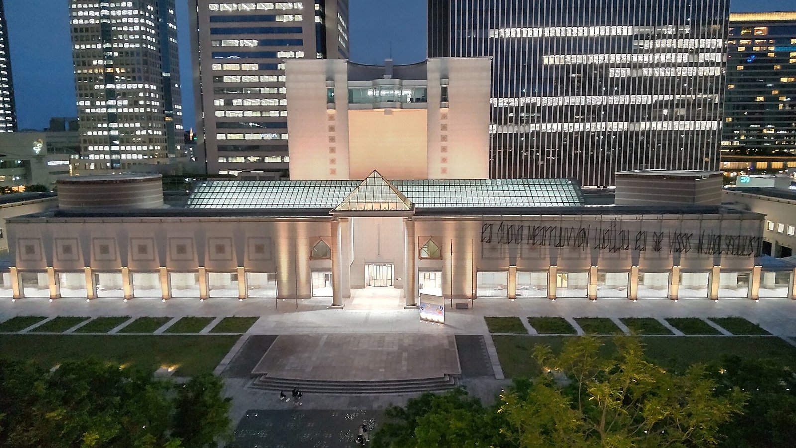 夜、ライトアップされた横浜美術館の正面。柱の並ぶ回廊と三角形のガラス屋根が光る