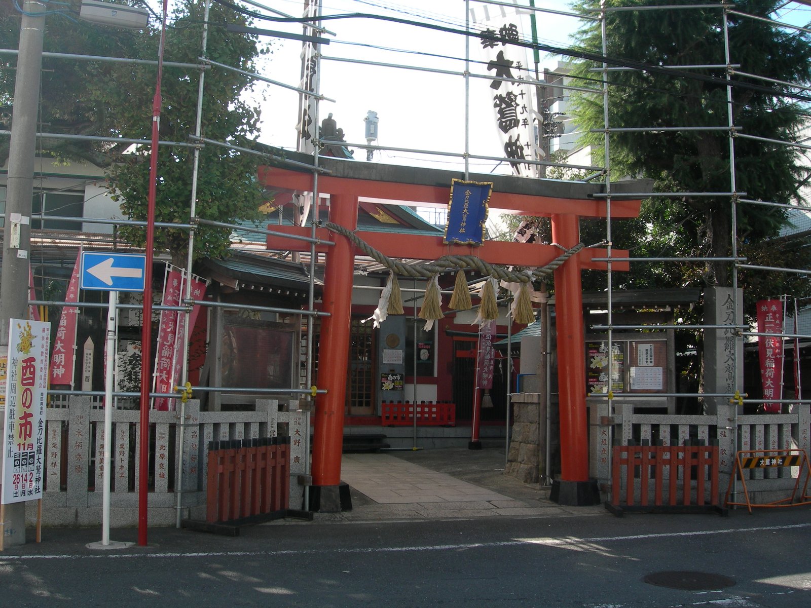 金刀比羅大鷲神社の朱色の鳥居。しめ縄が掛かり、左手前に「酉の市 11月」と書いた立て看板、鳥居の両脇に提灯を掛ける枠が組まれている