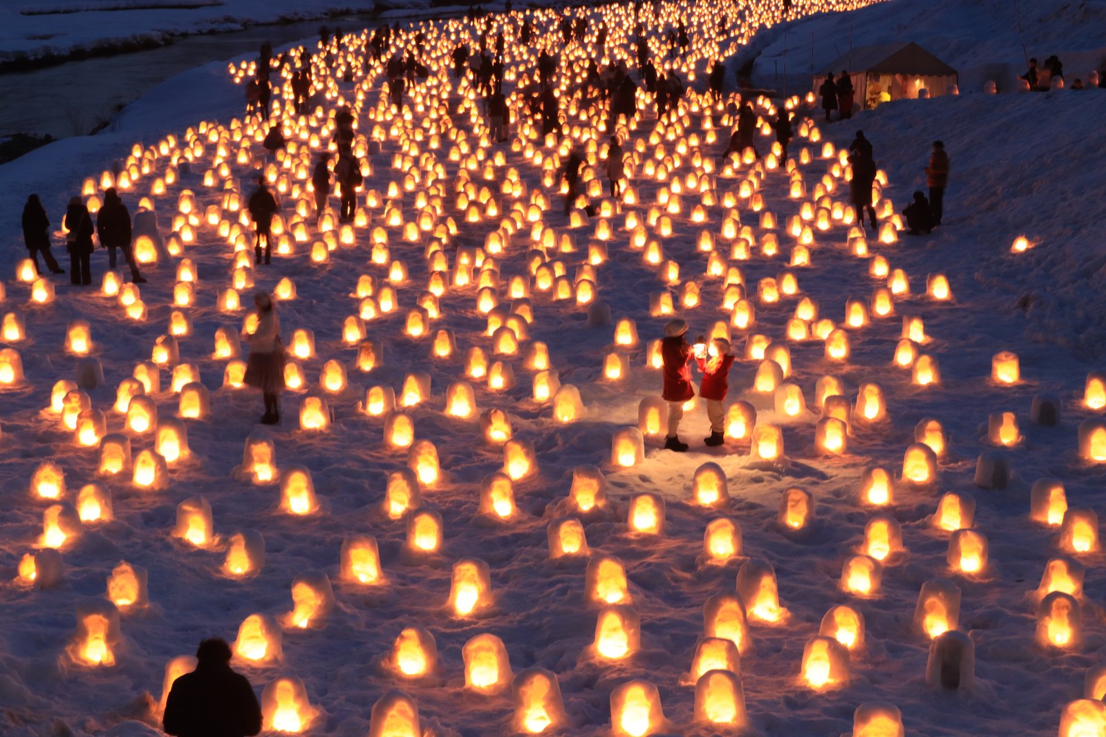 夕暮れの川原一面に、ろうそくの灯りの入った小さなかまくらが何百も並び、雪の上に見物の人影が点々とある