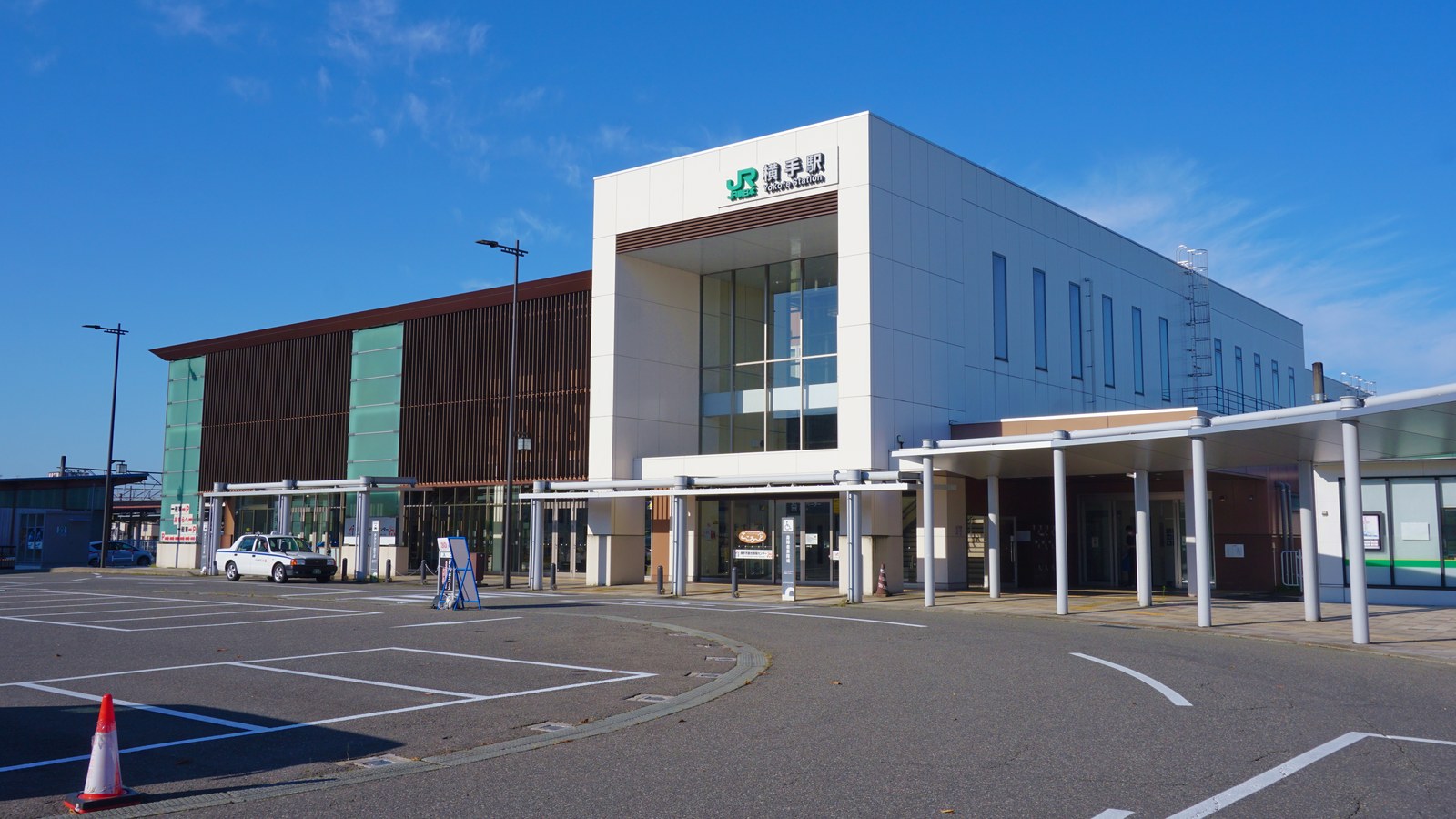 JR 横手駅の東口。白い箱形の駅舎の前にロータリーがあり、屋根付きの通路がのびている