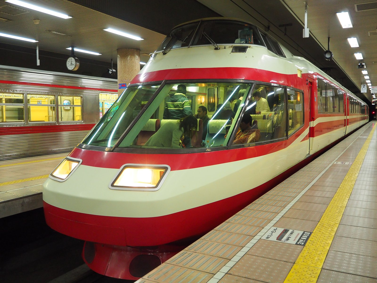 長野電鉄の地下駅ホームに停まる、白地に赤い帯の特急ゆけむり。先頭の大きな展望席に乗客が見え、左隣のホームには銀色の電車が停まっている