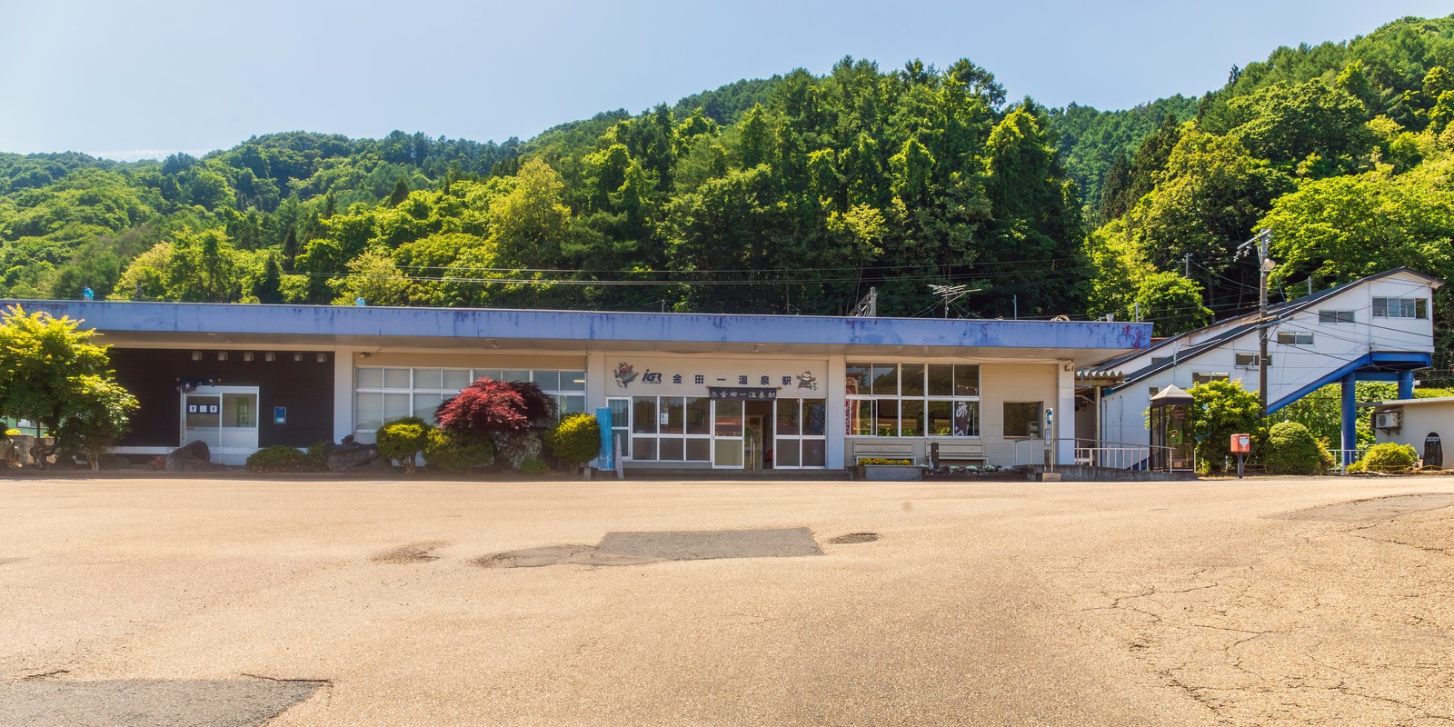 IGRいわて銀河鉄道の金田一温泉駅の駅舎外観。青い屋根の平屋建てで、正面に「金田一温泉駅」の看板、背後は緑の山、前は駐車場になっている