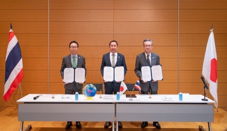 タイ王国との公式参加契約の調印後の記念撮影。左から越川政府委員、コートン・タイ陳列区域政府委員、河村事務総長。タイと日本の旗が立つ
