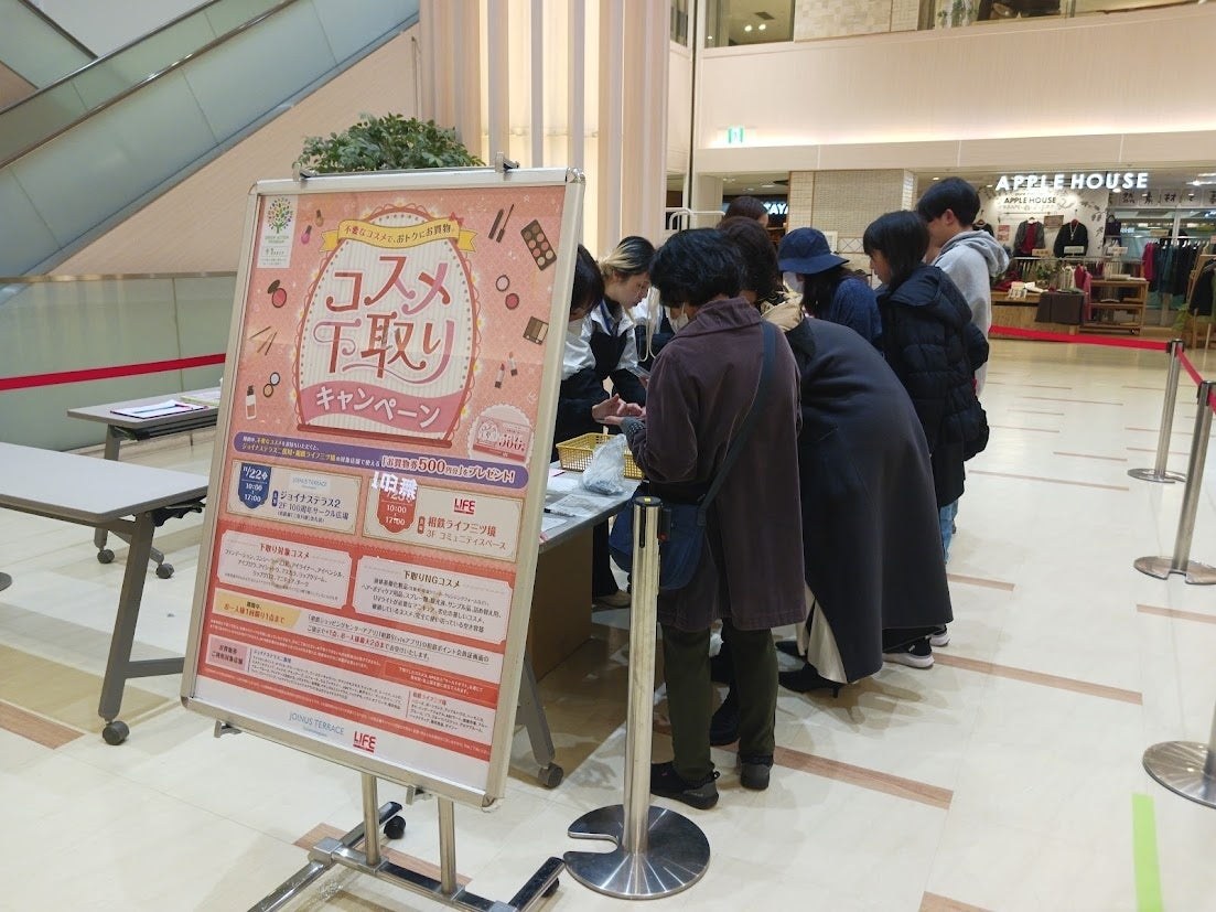 商業施設の吹き抜けに立てた「コスメ下取りキャンペーン」の案内板と、その奥の受付台に列を作る来店客