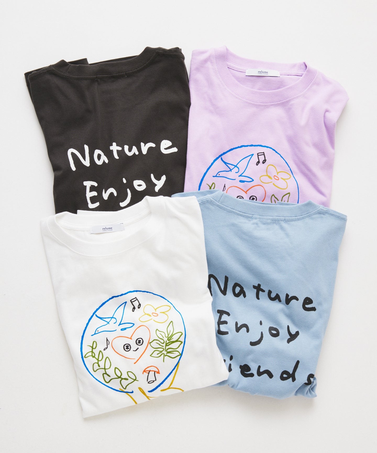 Long-sleeved T-shirts in black, lilac, white and pale blue laid in a stack. On the chest is a round drawing of Tunku Tunku's heart face with a bird, flowers and leaves, and the handwritten words Nature Enjoy Friends