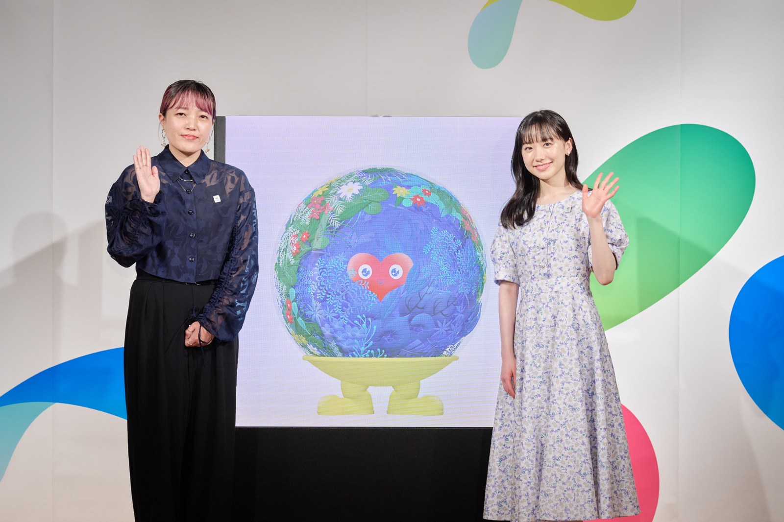 記者発表会の壇上。中央の画面にトゥンクトゥンクが映り、左に名前を考えた北原やえさん、右に公式アンバサダーの芦田愛菜さんが立って手を振っている